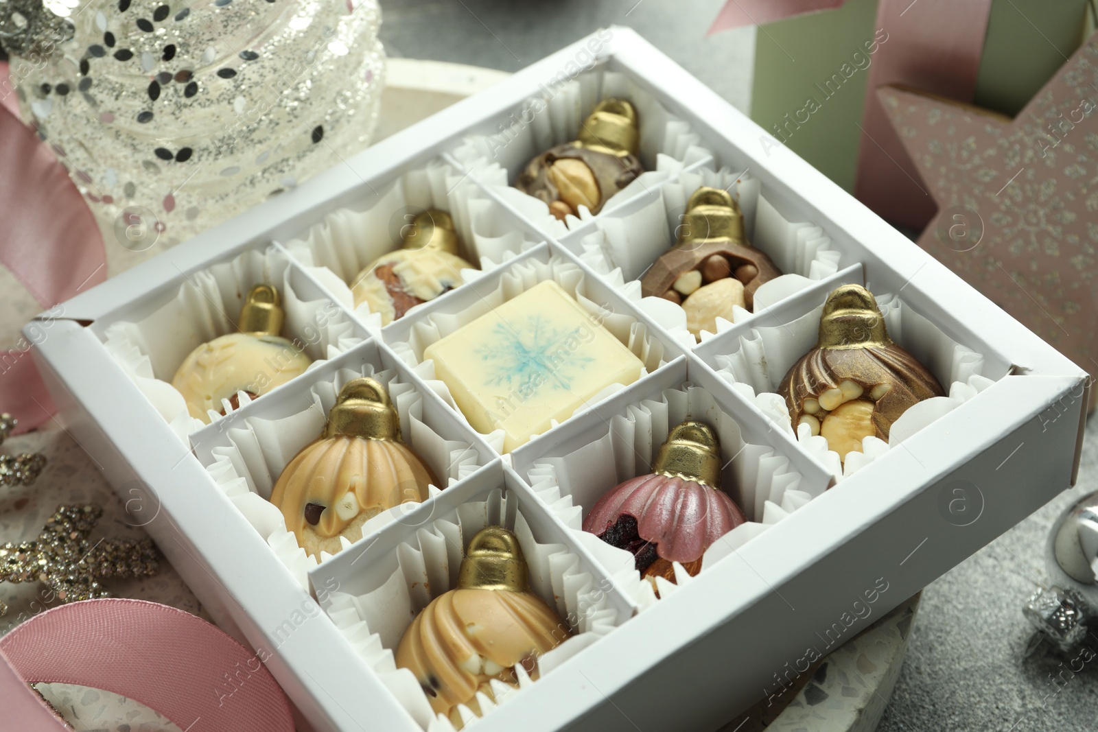 Photo of Box with tasty sweets in shape of baubles and Christmas decor on grey background, closeup