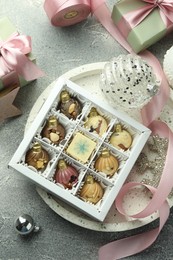 Photo of Box with tasty sweets in shape of baubles and Christmas decor on grey background, flat lay