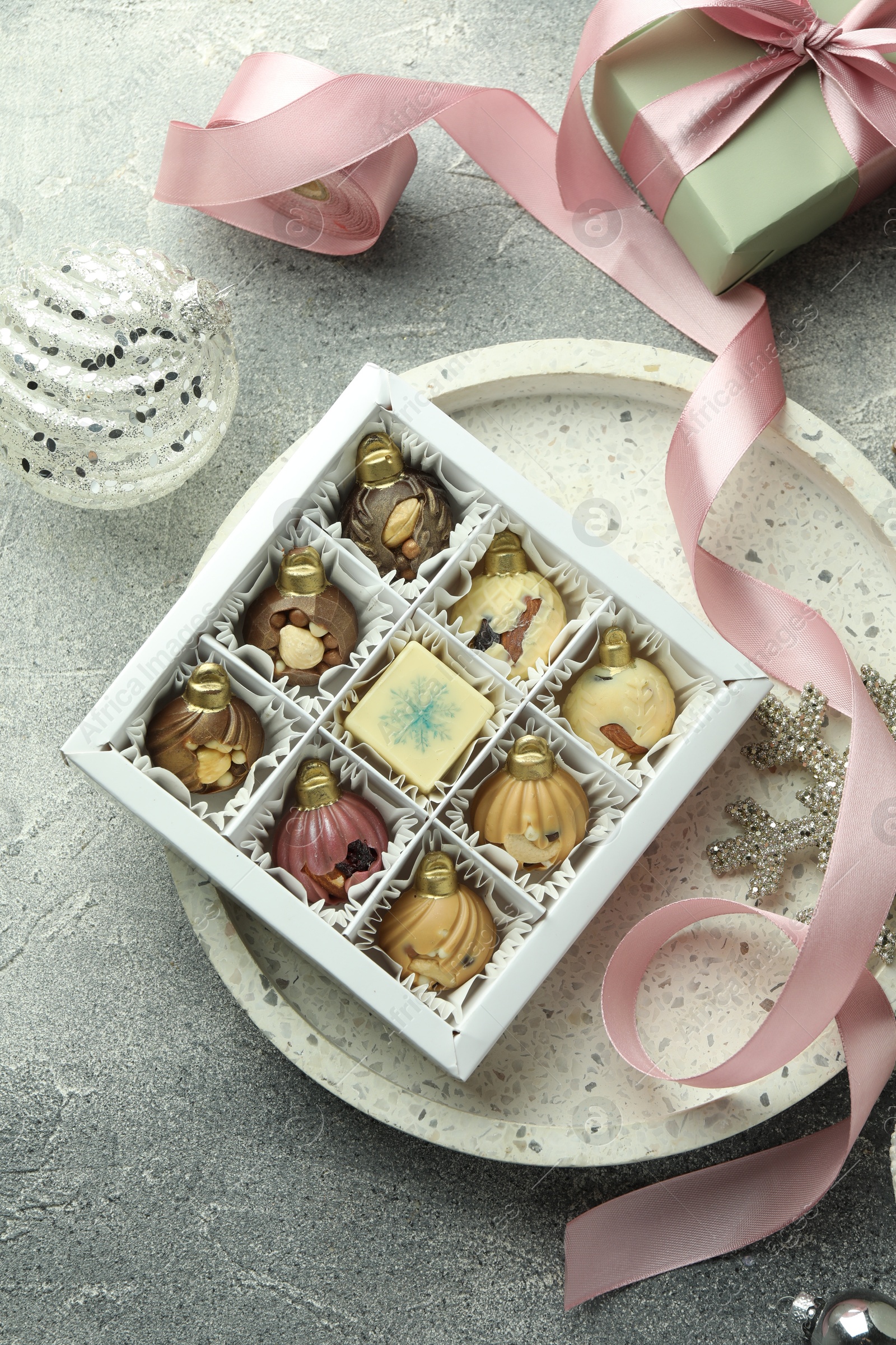 Photo of Box with tasty sweets in shape of baubles and Christmas decor on grey background, flat lay