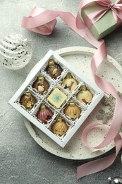 Photo of Box with tasty sweets in shape of baubles and Christmas decor on grey background, flat lay