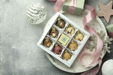 Photo of Box with tasty sweets in shape of baubles and Christmas decor on grey background, flat lay. Space for text