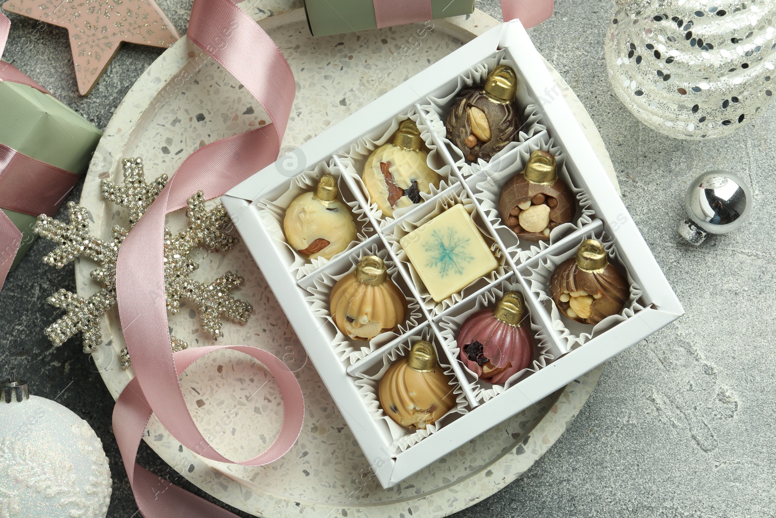 Photo of Box with tasty sweets in shape of baubles and Christmas decor on grey background, flat lay