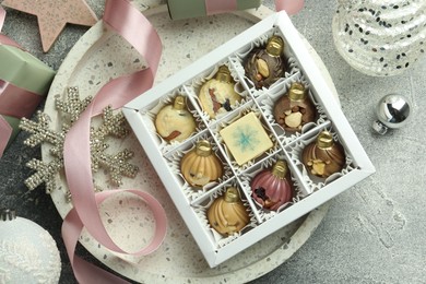 Photo of Box with tasty sweets in shape of baubles and Christmas decor on grey background, flat lay