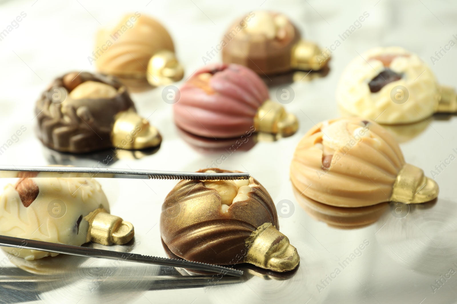 Photo of Tweezers with different sweets in shape of baubles on light table, closeup