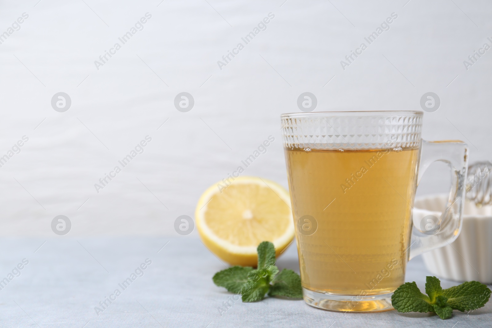 Photo of Aromatic mint tea in glass cup, fresh leaves and lemon on light gray table against white background, space for text