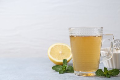 Photo of Aromatic mint tea in glass cup, fresh leaves and lemon on light gray table against white background, space for text