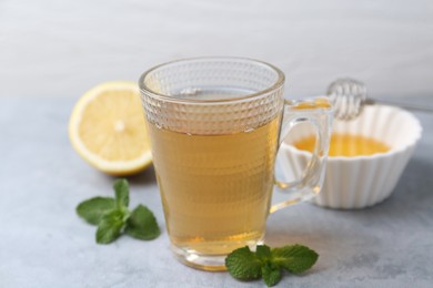 Photo of Aromatic mint tea in glass cup, fresh leaves and lemon on light gray table, closeup