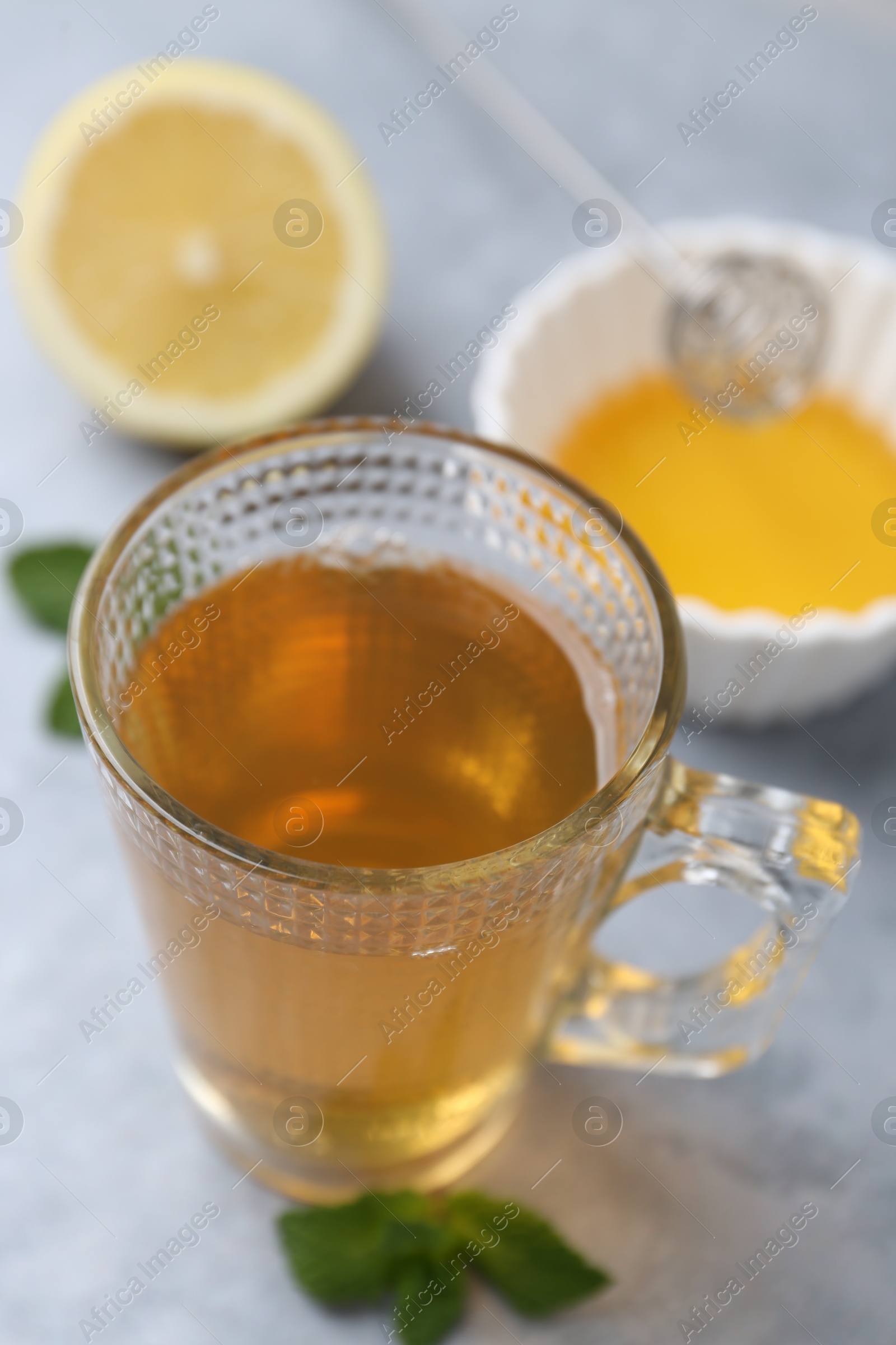 Photo of Aromatic mint tea in glass cup, fresh leaves, honey and lemon on light gray table, closeup