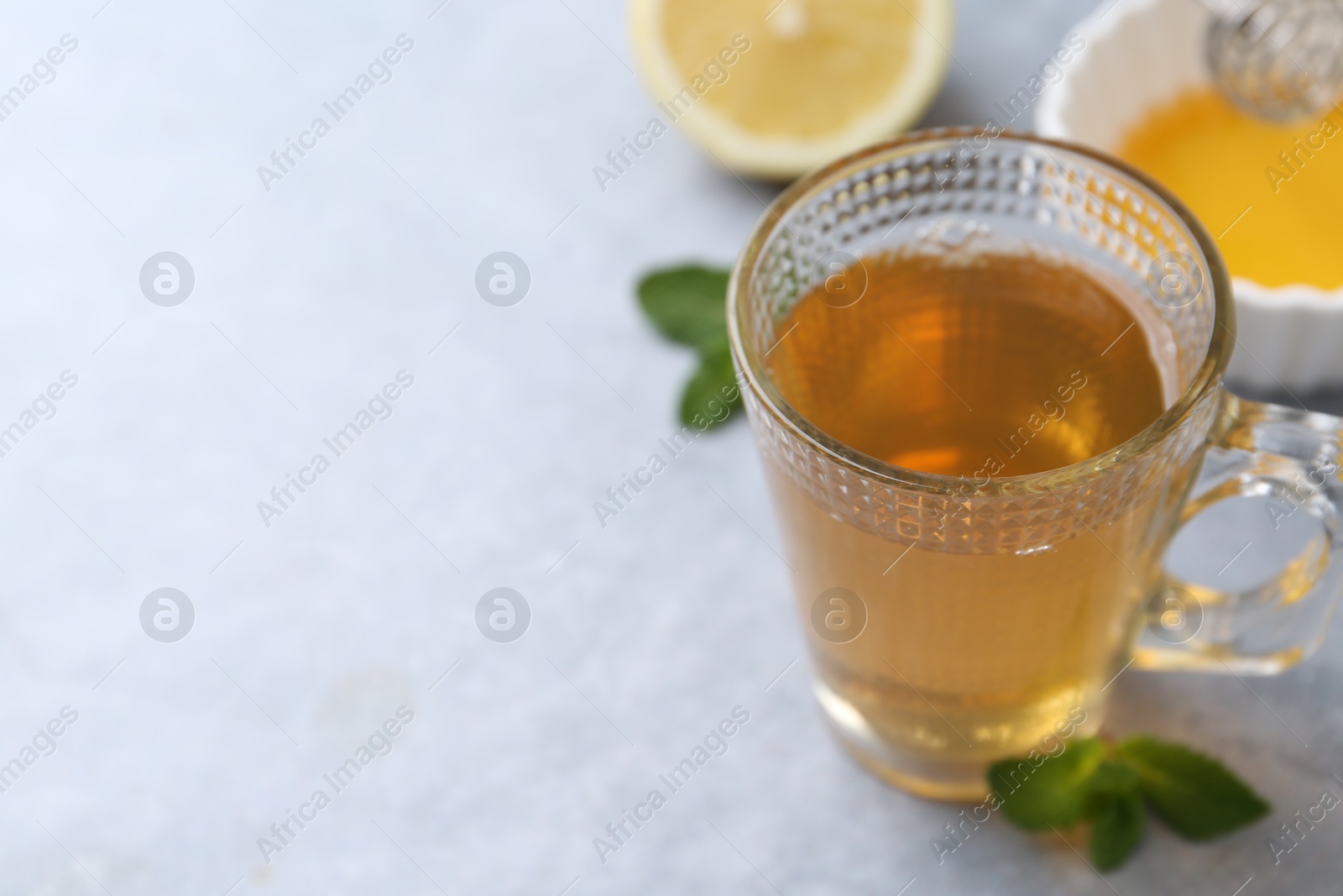 Photo of Aromatic mint tea in glass cup, fresh leaves, honey and lemon on light gray table, closeup. Space for text