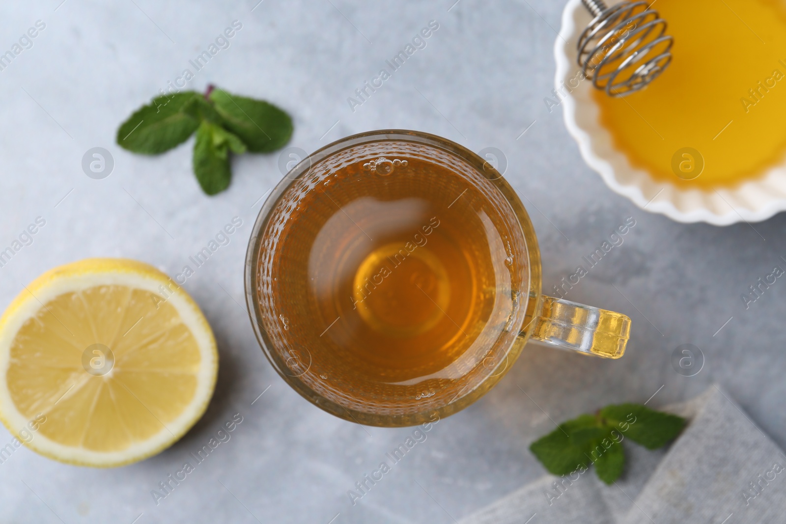 Photo of Aromatic mint tea in glass cup, fresh leaves, honey and lemon on light gray table, flat lay