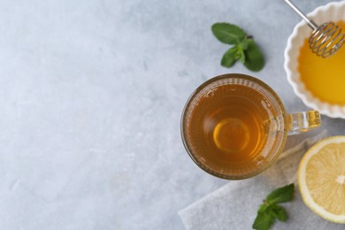 Photo of Aromatic mint tea in glass cup, fresh leaves, honey and lemon on light gray table, flat lay. Space for text