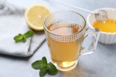 Photo of Aromatic mint tea in glass cup, fresh leaves, honey and lemon on light gray table, closeup