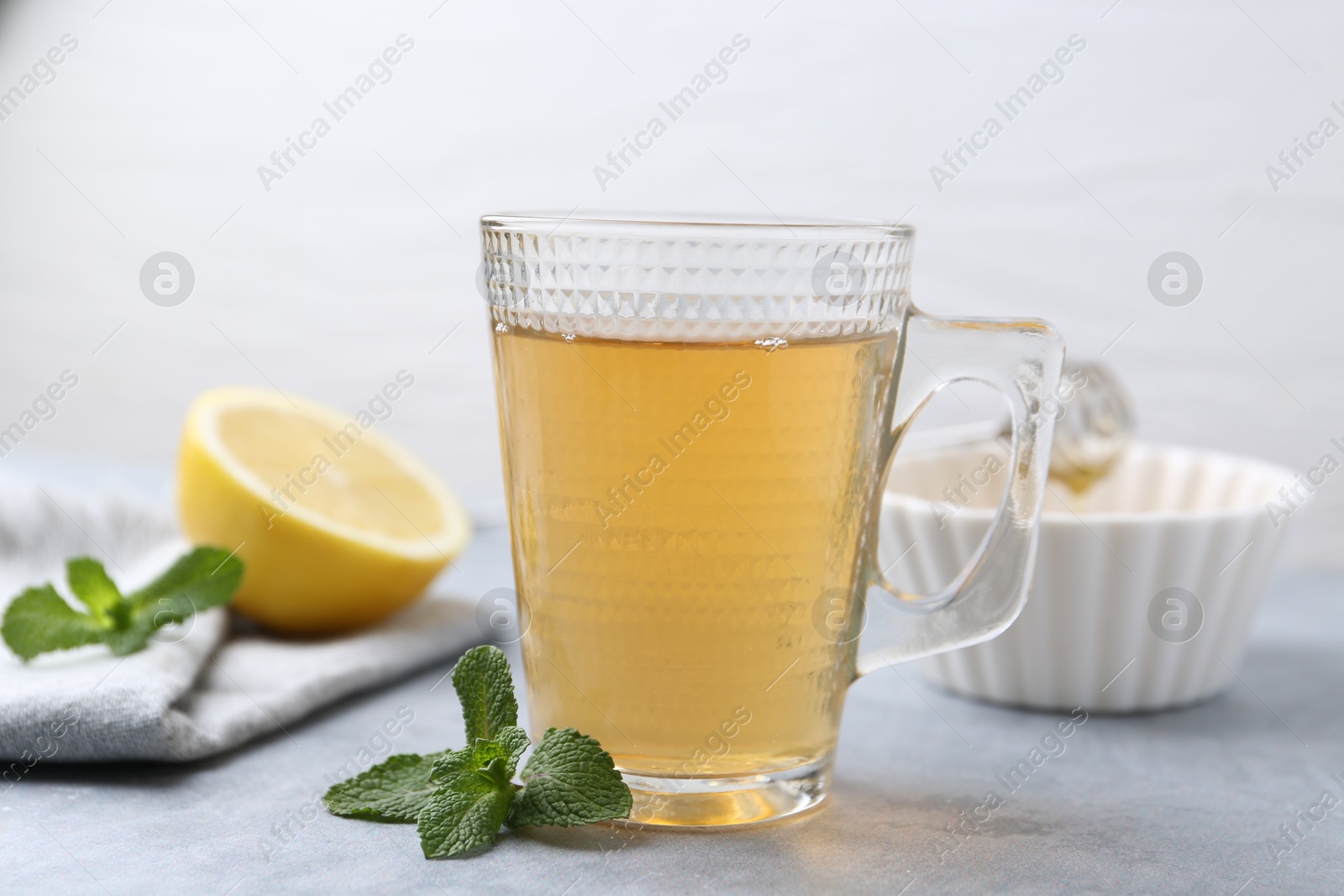 Photo of Aromatic mint tea in glass cup and fresh leaves on light gray table, closeup