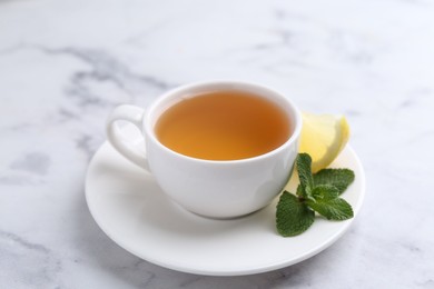 Photo of Aromatic mint tea in cup, fresh leaves and lemon on light marble table, closeup