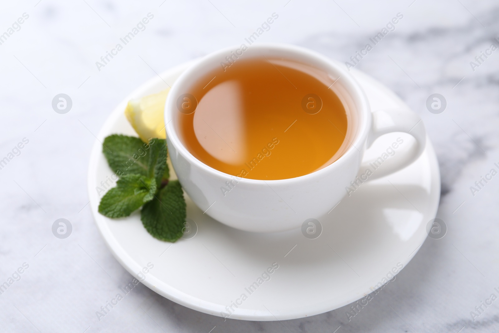 Photo of Aromatic mint tea in cup, fresh leaves and lemon on light marble table, closeup