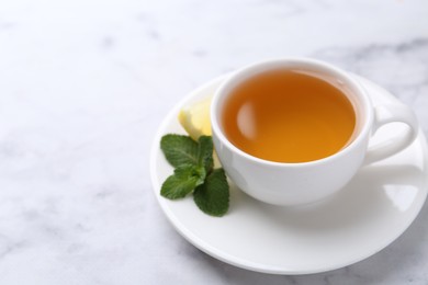 Photo of Aromatic mint tea in cup, fresh leaves and lemon on light table, closeup. Space for text