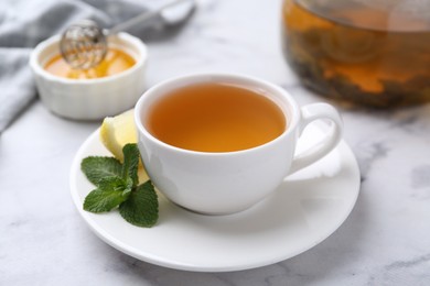 Photo of Aromatic mint tea in cup, fresh leaves and lemon on light marble table, closeup