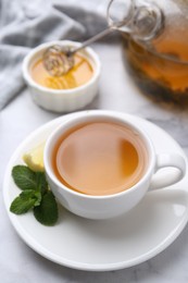 Photo of Aromatic mint tea in cup, fresh leaves, lemon and honey on light table, closeup