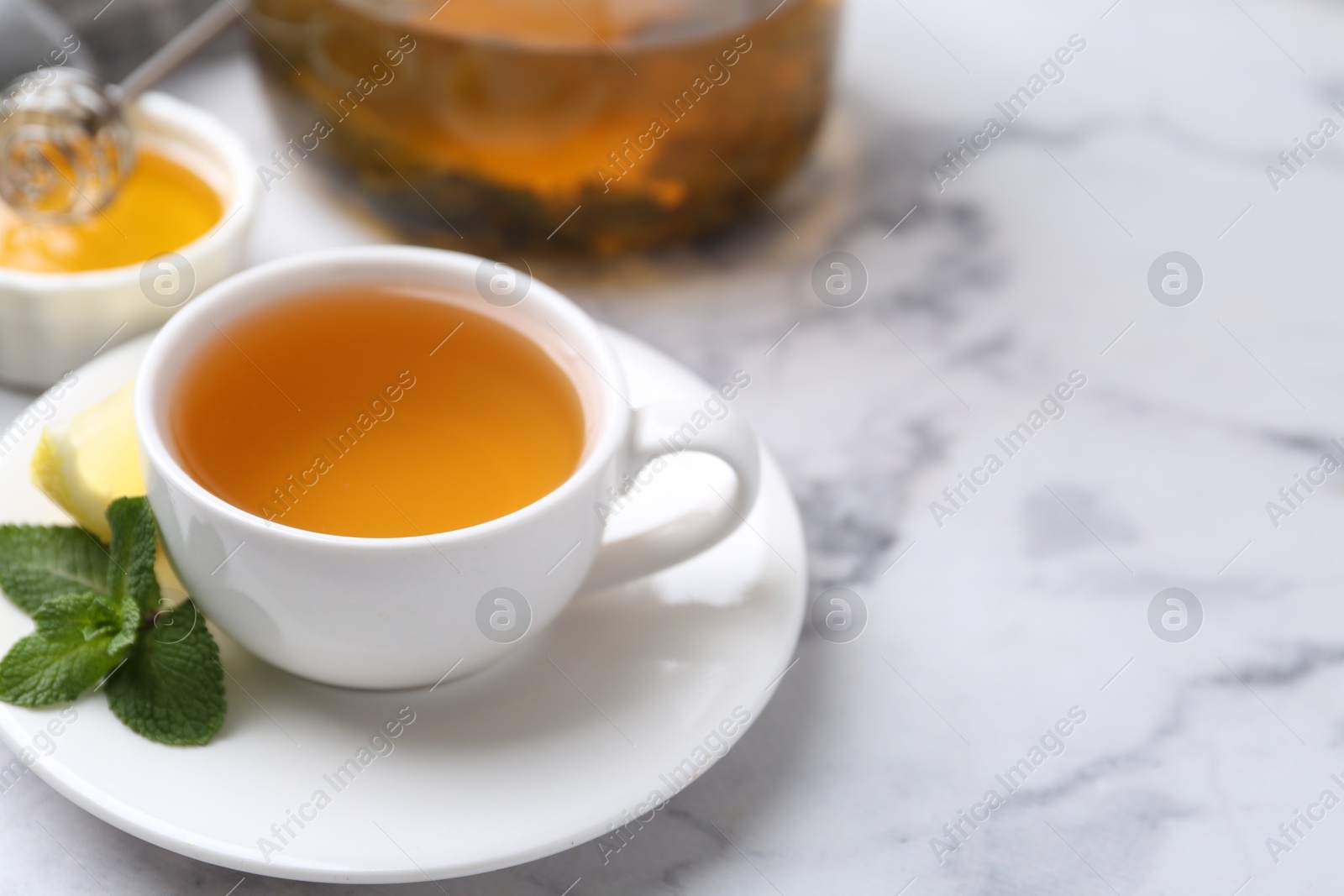 Photo of Aromatic mint tea in cup, fresh leaves and lemon on light marble table, closeup. Space for text