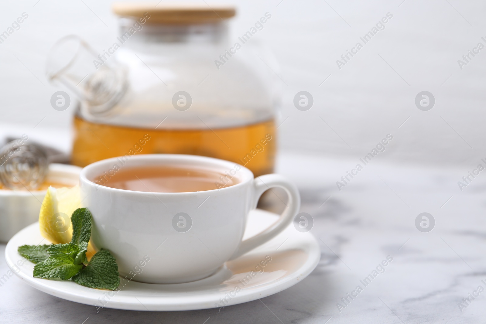 Photo of Aromatic mint tea in cup, fresh leaves and lemon on light marble table, space for text