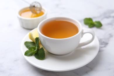 Photo of Aromatic mint tea in cup, fresh leaves and lemon on light marble table, closeup