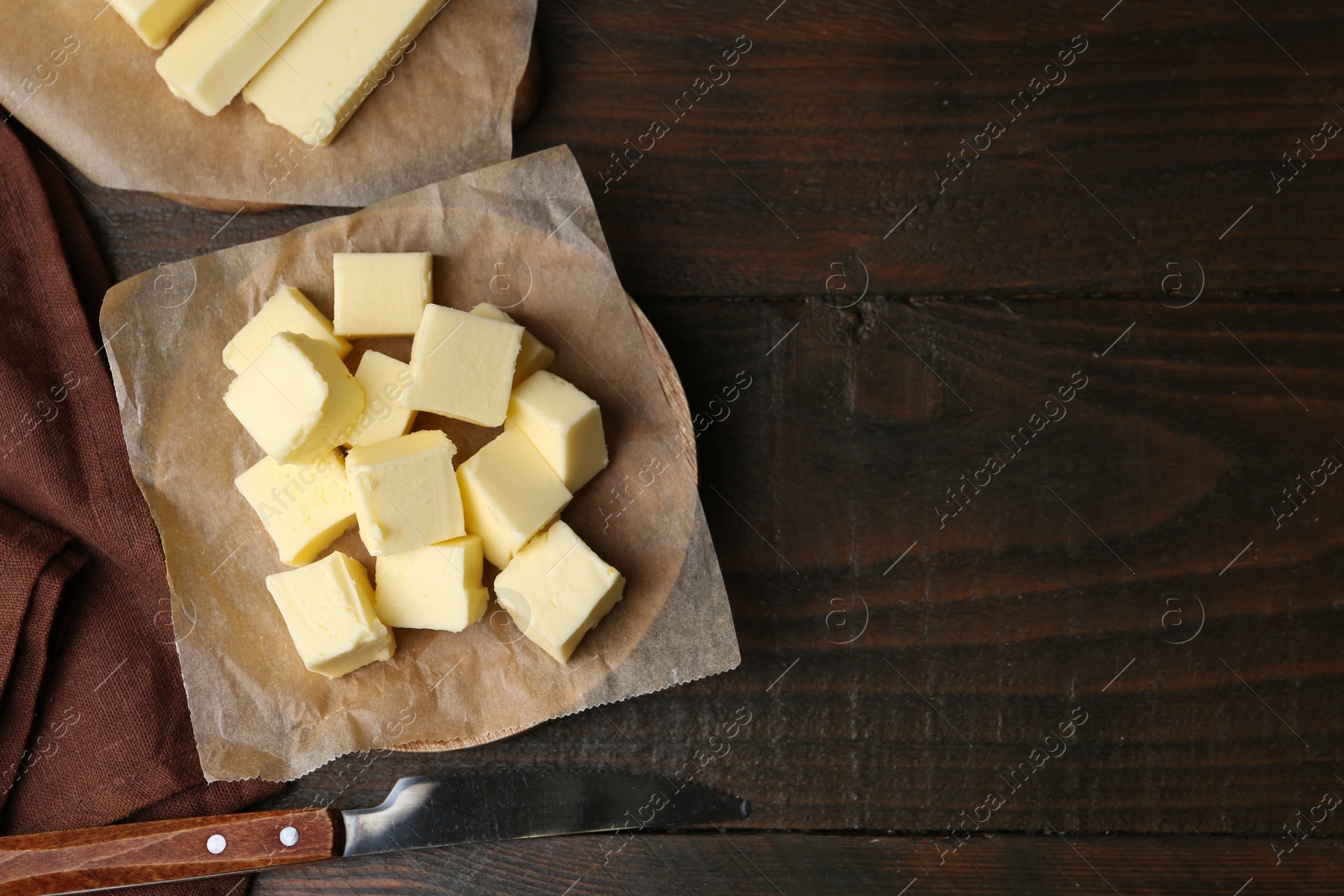 Photo of Pieces of fresh butter and knife on wooden table, flat lay. Space for text