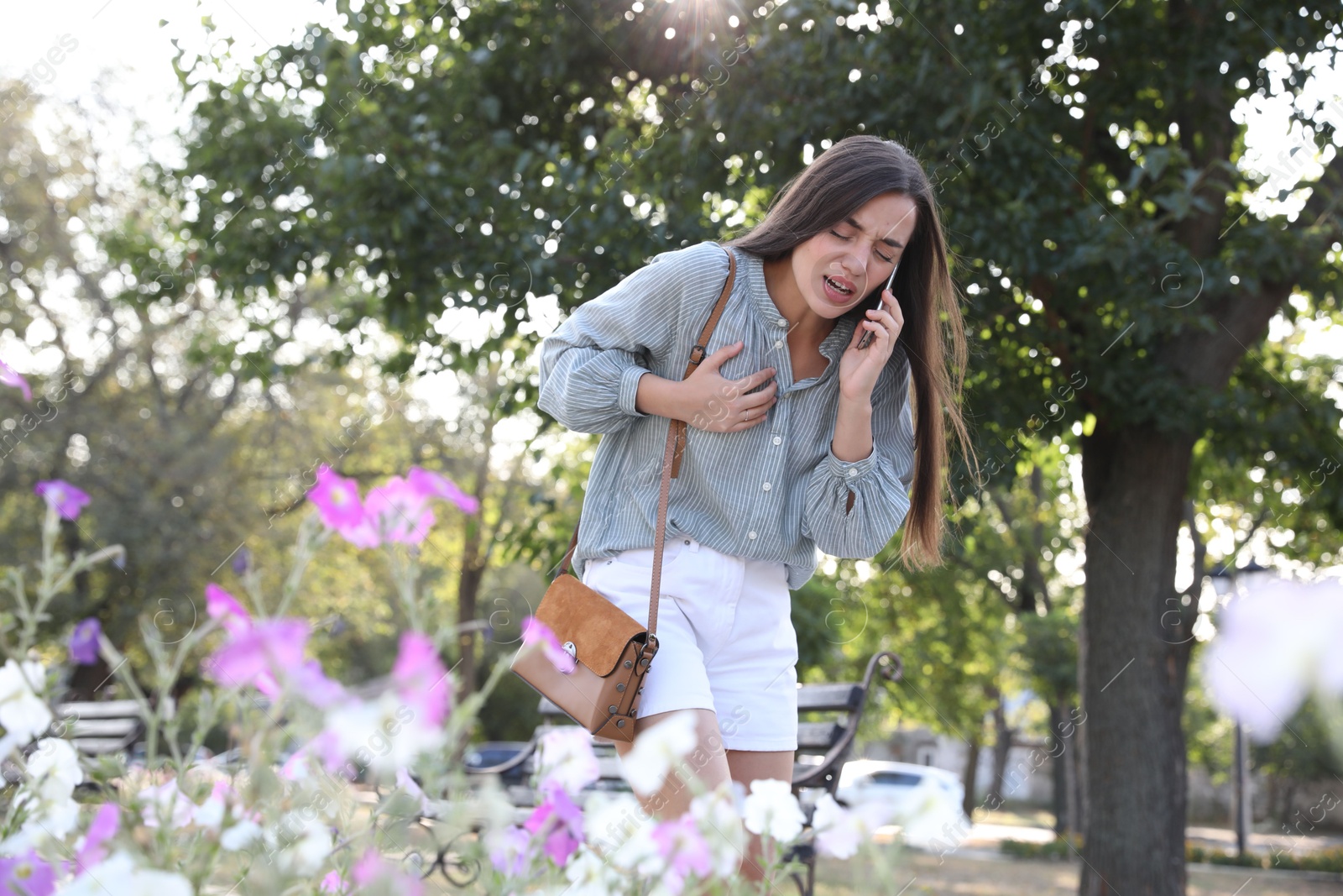 Photo of Young woman with heart attack calling ambulance in park