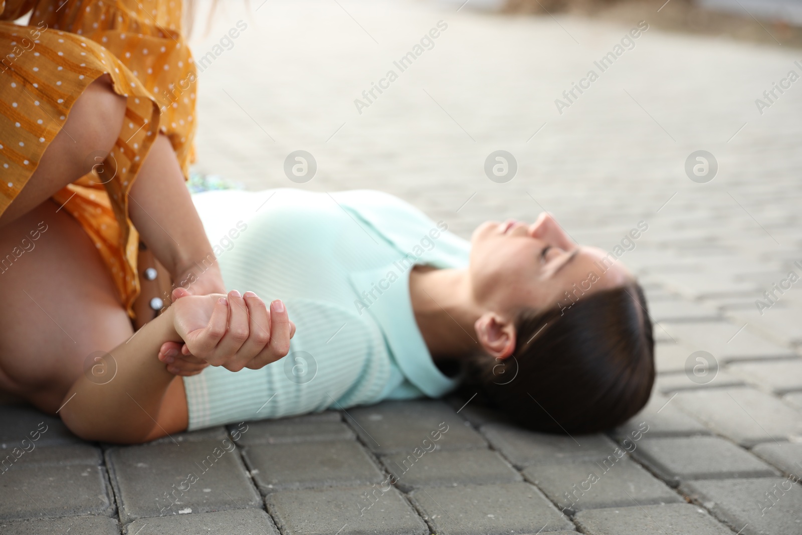 Photo of Woman checking pulse of unconscious person with heart attack on city street