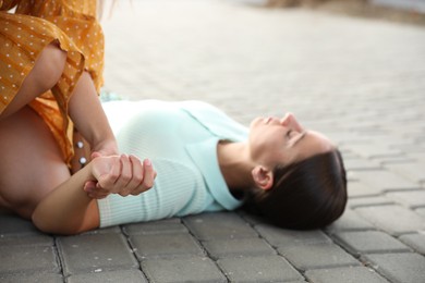 Woman checking pulse of unconscious person with heart attack on city street