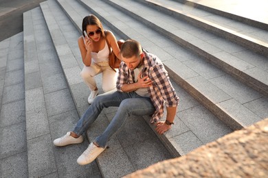 Woman calling ambulance to help man with heart attack on stairs