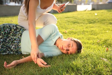 Photo of Woman checking pulse of unconscious person with heart attack in park, closeup