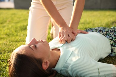 Photo of Woman doing cardiac massage to unconscious person with heart attack on green lawn