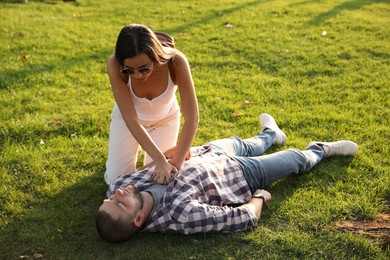 Woman doing cardiac massage to unconscious man with heart attack on green lawn