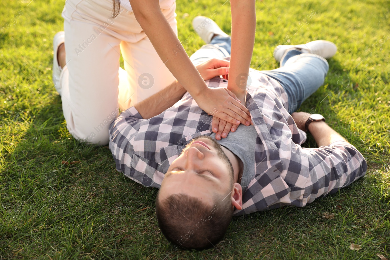 Photo of Woman doing cardiac massage to unconscious man with heart attack on green lawn