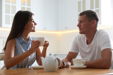 Photo of Man and woman talking while drinking tea at table in kitchen