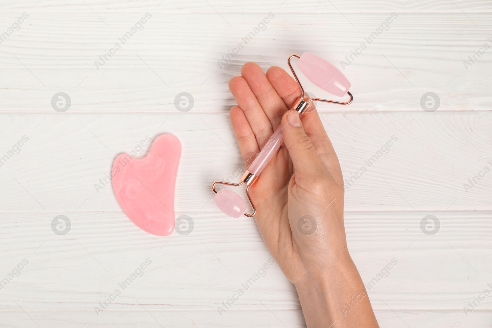 Photo of Woman with face roller and gua sha tool on white wooden background, top view