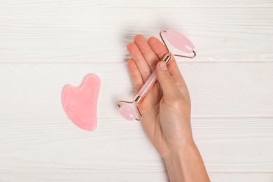 Photo of Woman with face roller and gua sha tool on white wooden background, top view