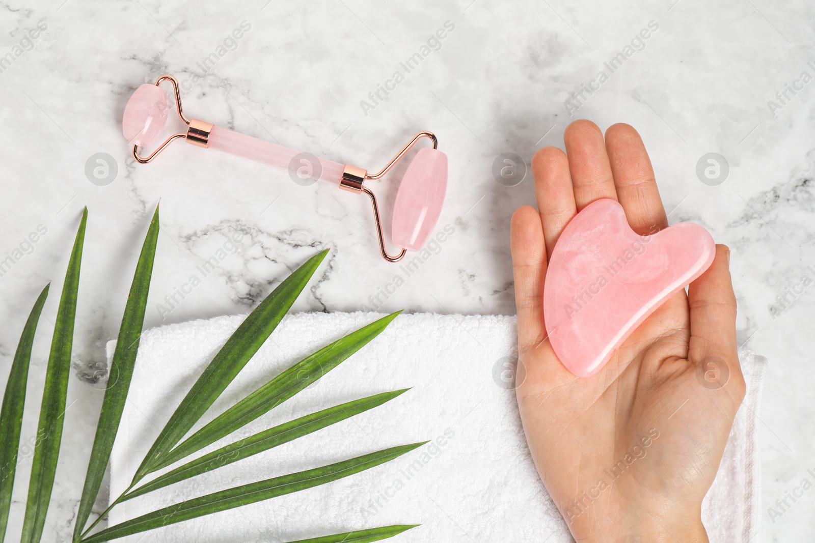 Photo of Woman with gua sha tool and face roller on white marble background, top view