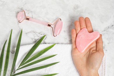 Photo of Woman with gua sha tool and face roller on white marble background, top view