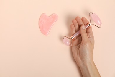 Photo of Woman with face roller and gua sha tool on beige background, top view. Space for text