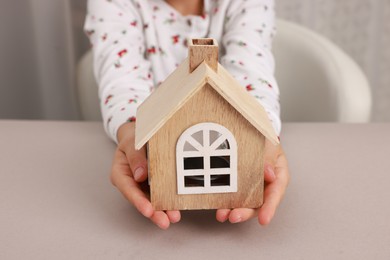 Photo of Adoption. Little girl with house figure at beige table, closeup