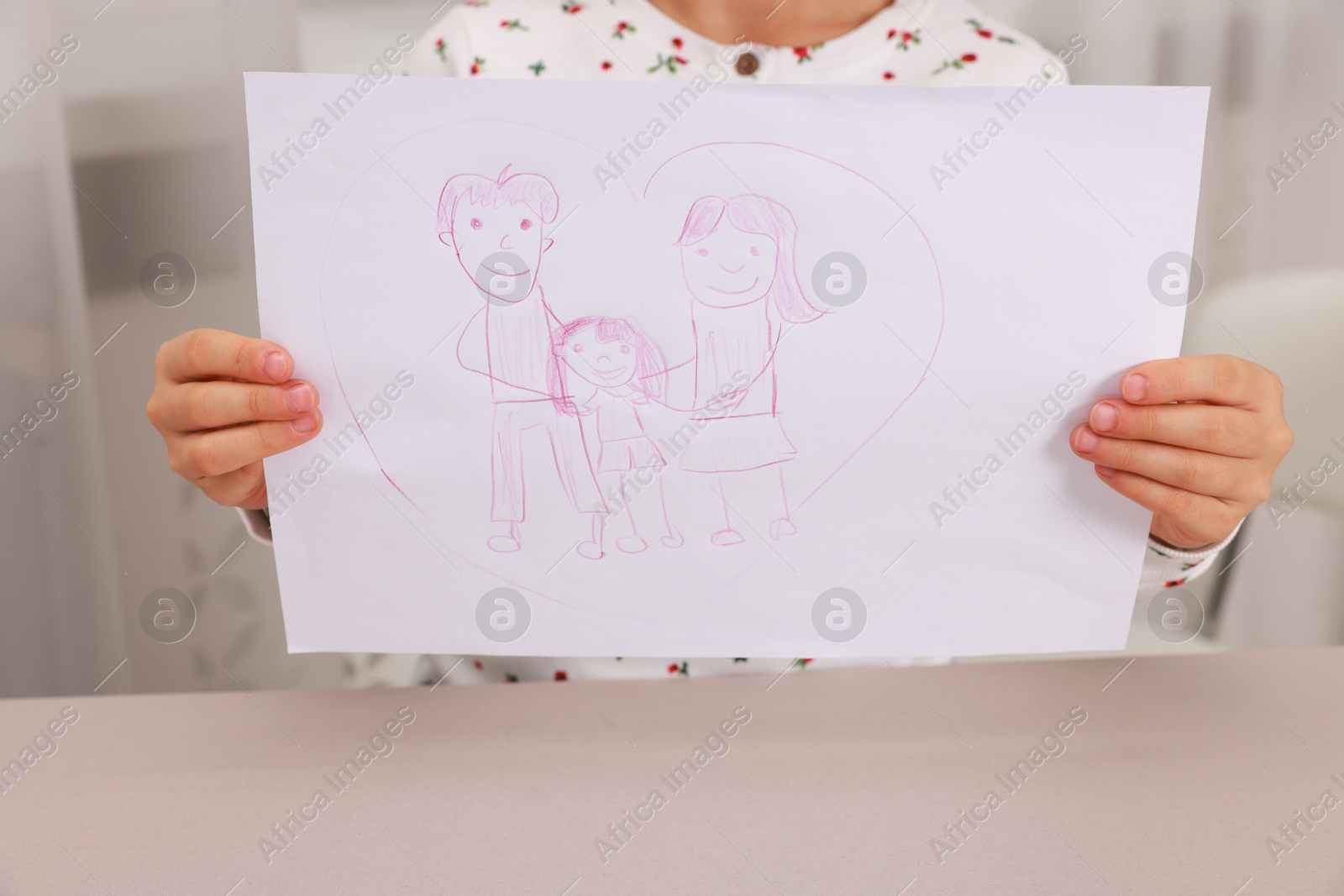 Photo of Adoption. Little girl holding drawing of family at beige table, closeup