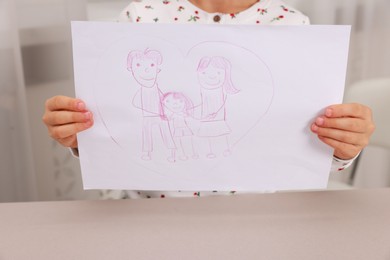 Photo of Adoption. Little girl holding drawing of family at beige table, closeup