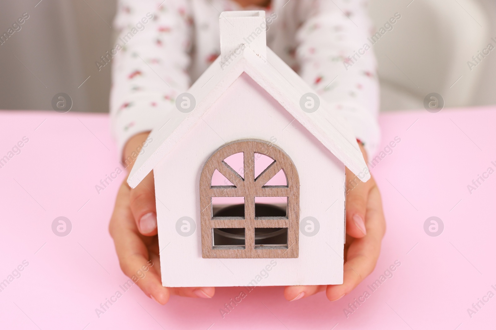 Photo of Adoption. Little girl with house figure at pink table, closeup