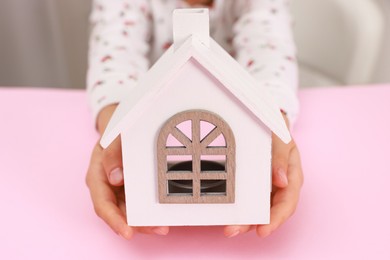 Photo of Adoption. Little girl with house figure at pink table, closeup