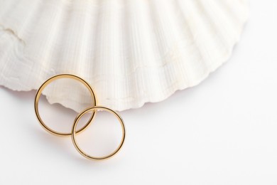 Photo of Beautiful golden wedding rings and sea shell on white background, top view