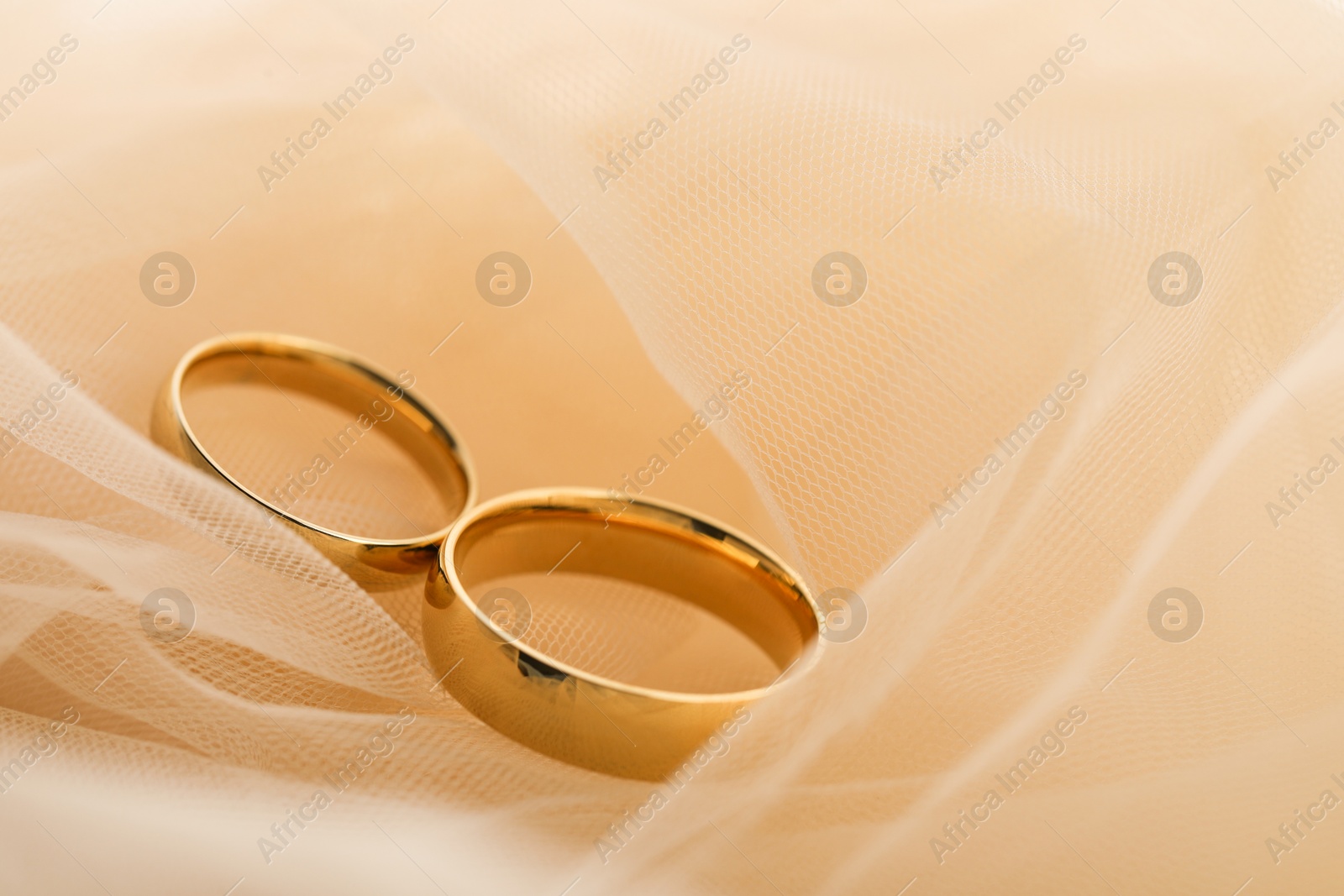 Photo of Beautiful golden wedding rings on beige fabric, closeup