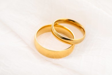 Photo of Beautiful golden wedding rings on white fabric, closeup