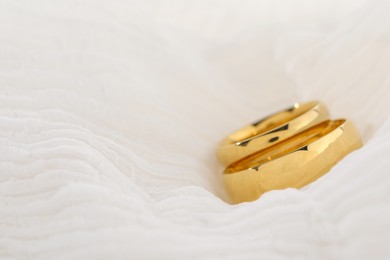 Photo of Beautiful golden wedding rings on white fabric, closeup. Space for text