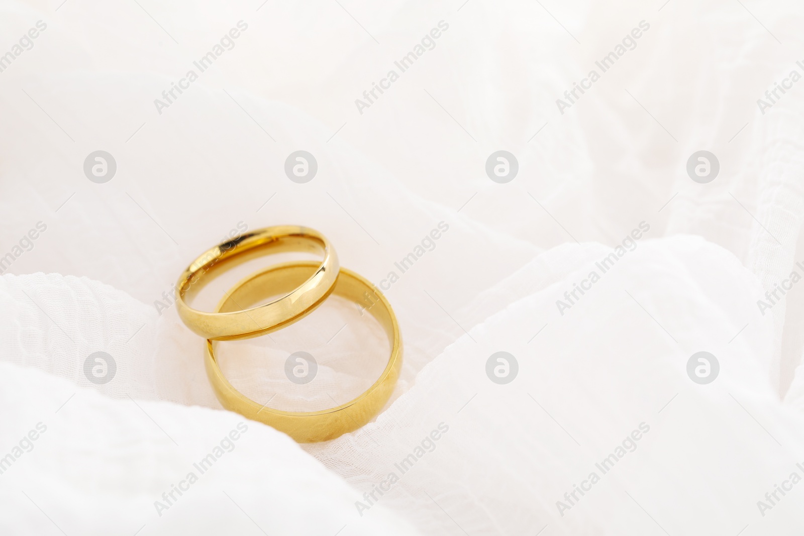 Photo of Beautiful golden wedding rings on white fabric, space for text